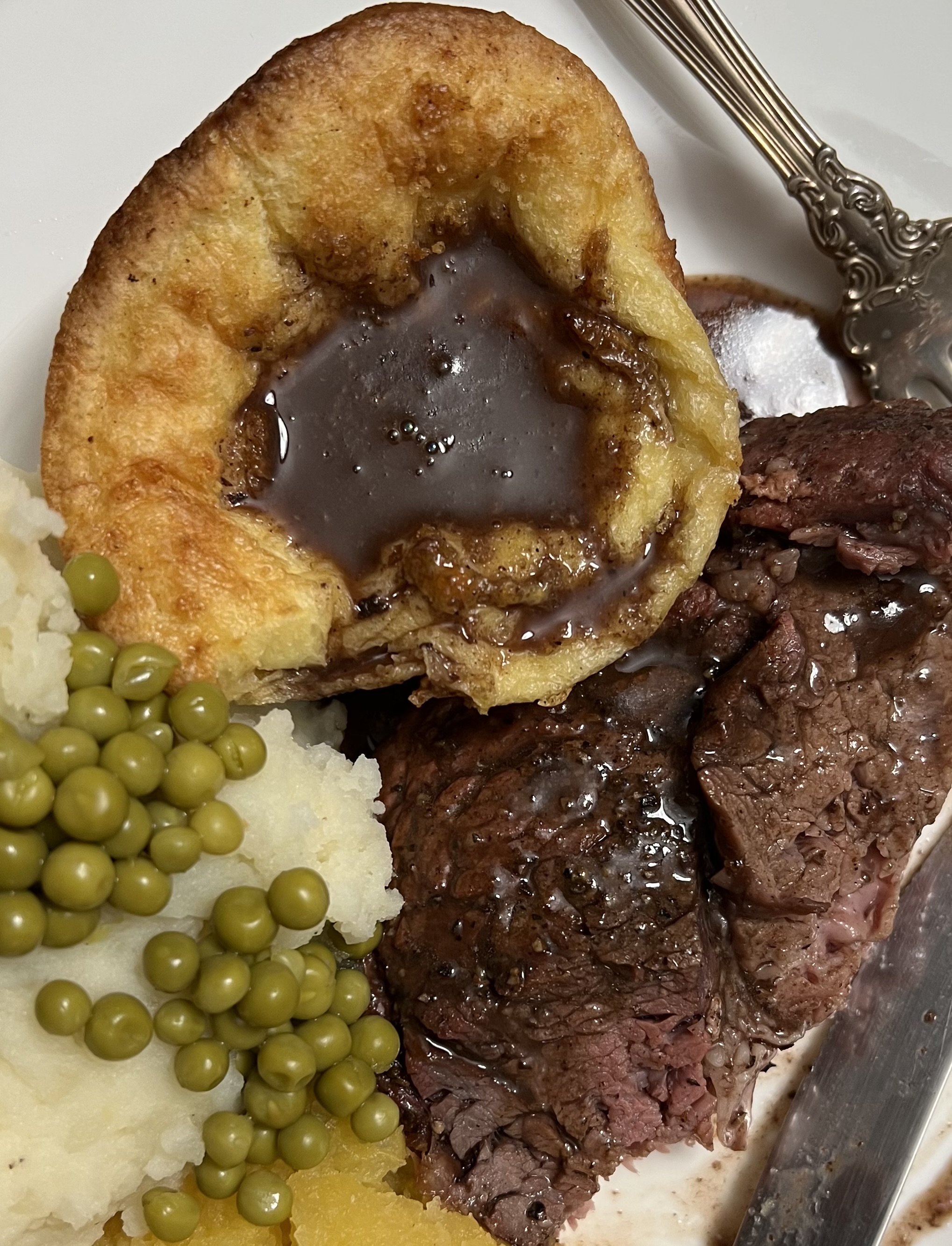 Red wine beef gravy over sliced beef, yorkshire pudding, mashed potatoes and peas